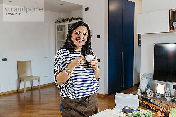 Lächelnde Frau mit Kaffeetasse  die zu Hause am Tisch steht