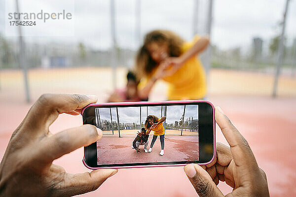 Man photographing friends through smart phone at sports court
