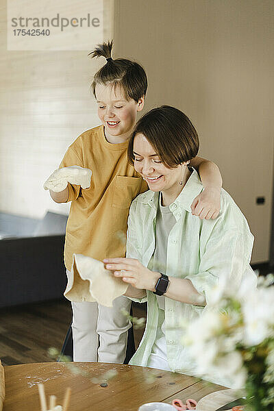 Smiling mother and son holding pizza doughs at home