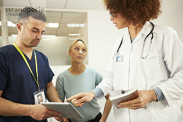 Krankenschwester und Arzt diskutieren über Tablet-PC mit älterem Patienten im Krankenzimmer
