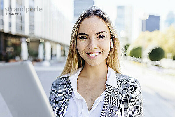 Lächelnde berufstätige Frau mit Tablet-PC und kabellosen In-Ear-Kopfhörern