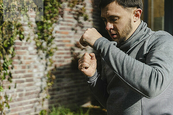 Young man practicing punching by ivy wall