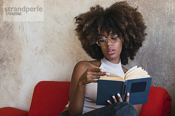 Young woman with afro hairstyle reading book at home