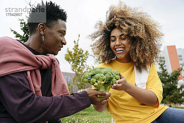 Young man giving broccoli to friend in park