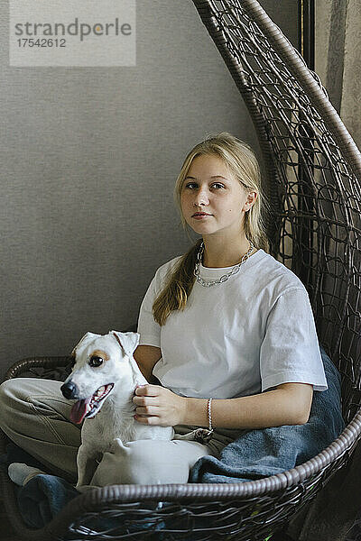 Teenager-Mädchen sitzt mit Hund auf Hängesessel zu Hause