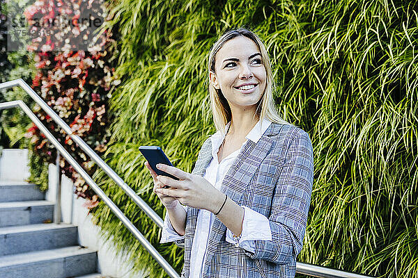 Young smiling working woman with smart phone in front of plants