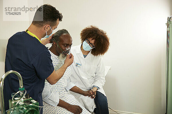 Nurse adjusting oxygen mask of patient with doctor in medical room