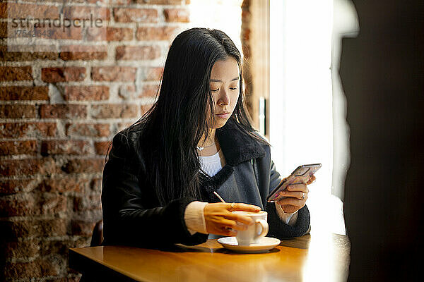 Junge Frau benutzt Mobiltelefon am Cafétisch