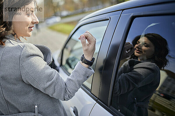 Frau in Jacke öffnet Armbanduhr mit Autotür