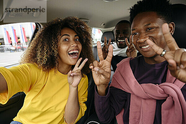 Happy multiracial friends gesturing peace sign in car enjoying road trip