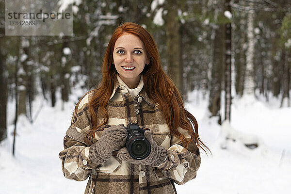 Happy woman with camera in winter forest