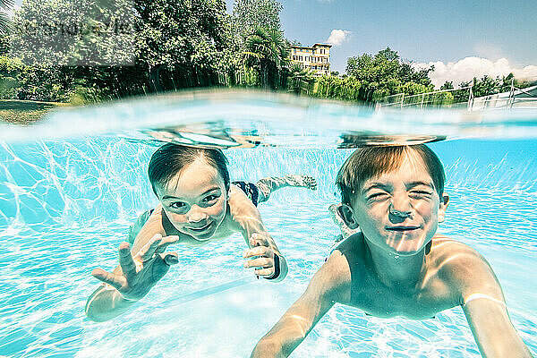 Smiling siblings swimming underwater in pool on sunny day