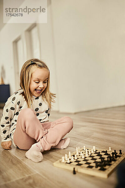 Happy girl sitting cross-legged looking at chessboard at home