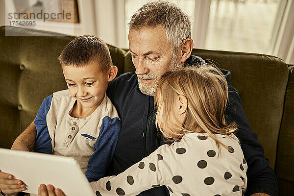 Enkelkinder sitzen mit Großvater zu Hause am Tablet-PC