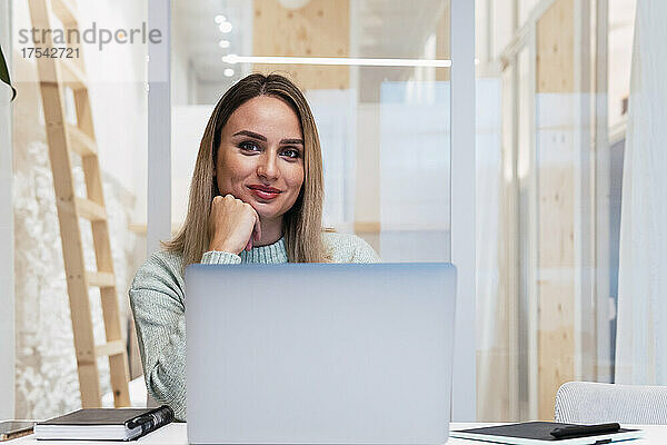 Berufstätige Frau mit Hand am Kinn hinter Laptop im Studio