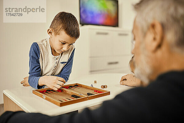 Konzentrierter Junge spielt zu Hause mit Großvater Backgammon