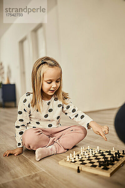 Curious girl sitting cross-legged pointing at chess board