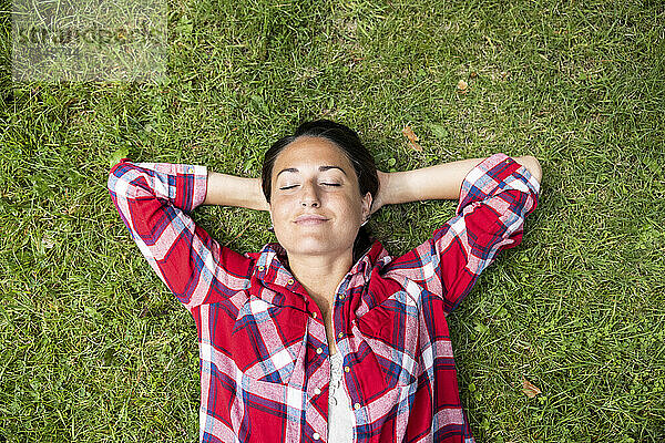 Frau entspannt sich im Gras mit geschlossenen Augen und Händen hinter dem Kopf