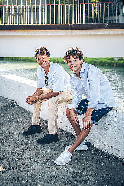 Smiling brothers sitting on wall by river