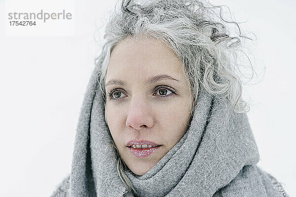 Nachdenkliche Frau mit Schnee auf den Lippen  in einen grauen Schal gehüllt