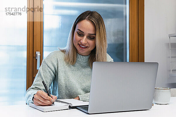 Geschäftsfrau schreibt mit Laptop Tagebuch auf dem Schreibtisch im Studio