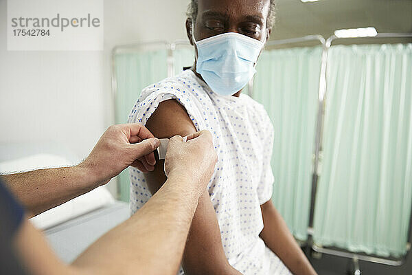 Krankenschwester mit Pflaster am Arm des Patienten im Krankenzimmer
