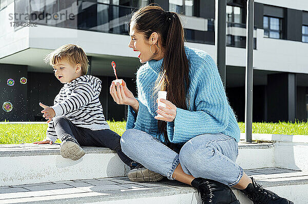 Cheerful mother and son playing with soap bubbles on sunny day