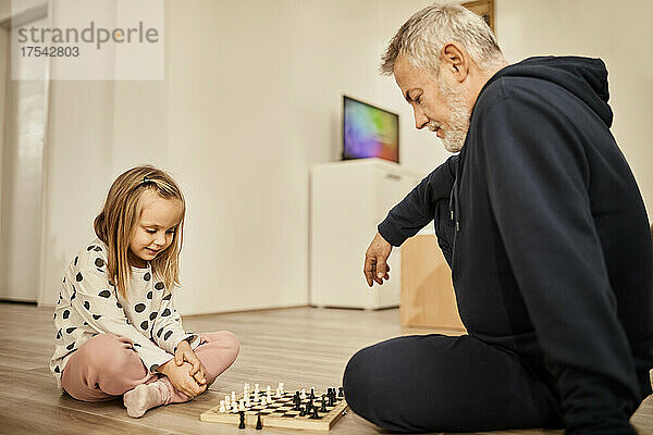 Granddaughter and grandfather playing chess at home