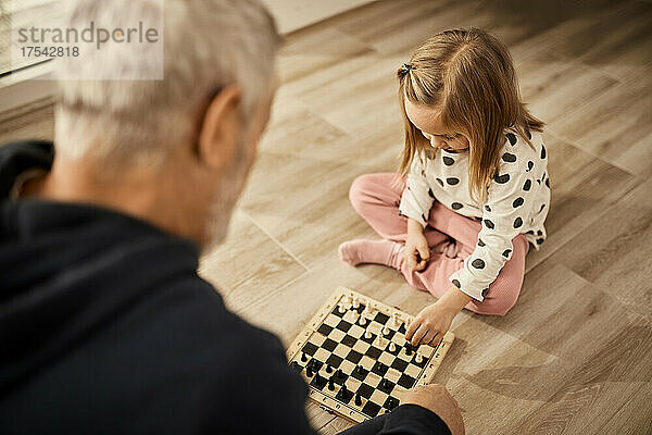 Granddaughter playing chess with grandfather sitting at home