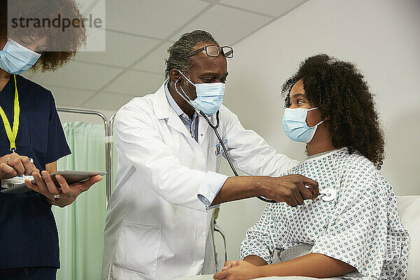 Doctor examining patient standing with female nurse in medical room