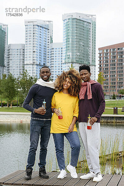 Young friends with lemonade bottles standing on jetty in urban park