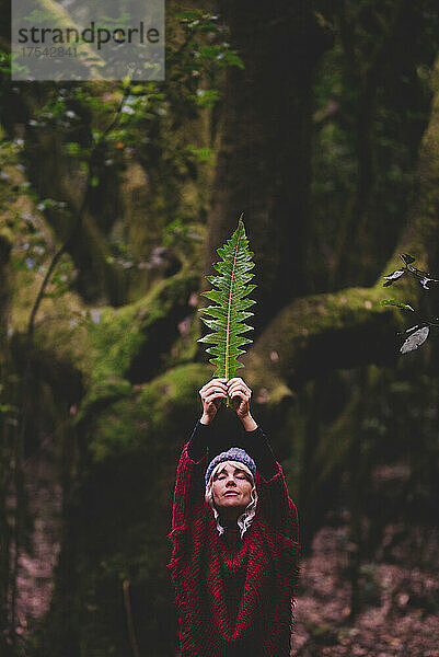Woman with hands raised holding leaf in forest