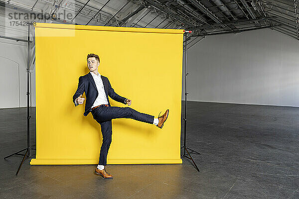 Businessman standing on one leg raising foot in front of yellow backdrop