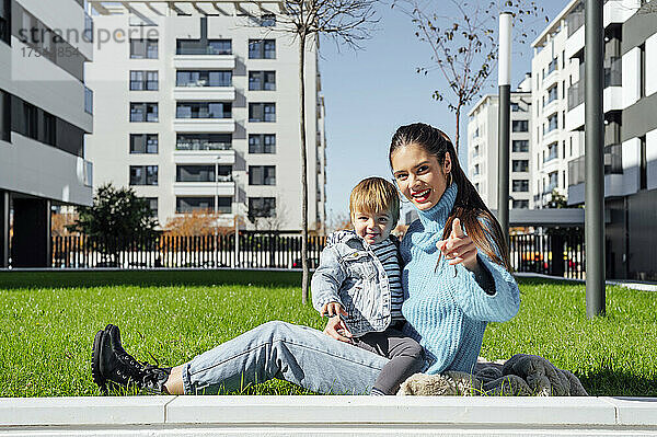 Lächelnde Mutter mit Sohn sitzt im Gras in der Stadt
