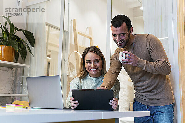 Glückliche Geschäftskollegen teilen sich einen Tablet-PC und arbeiten im Studio