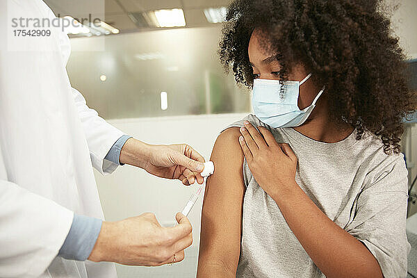 Girl with protective face mask taking COVID-19 vaccination at hospital