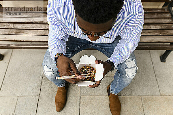 Young man having food sitting on bench