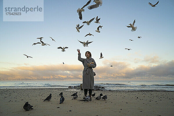 Woman feeding seagulls and pigeons at beach