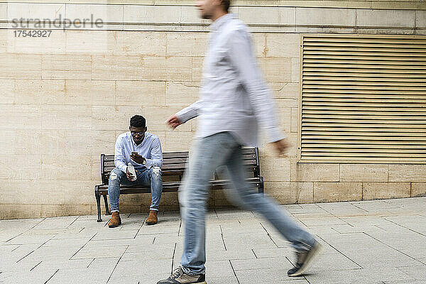 Junger Mann benutzt Smartphone auf Bank sitzend