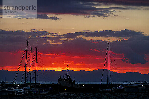 Italy  Province of South Sardinia  Villasimius  Silhouettes of boats moored in coastal harbor at red moody sunset