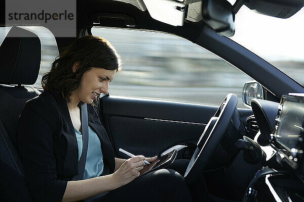 Lächelnde Geschäftsfrau nutzt Tablet-PC im autonom fahrenden Auto