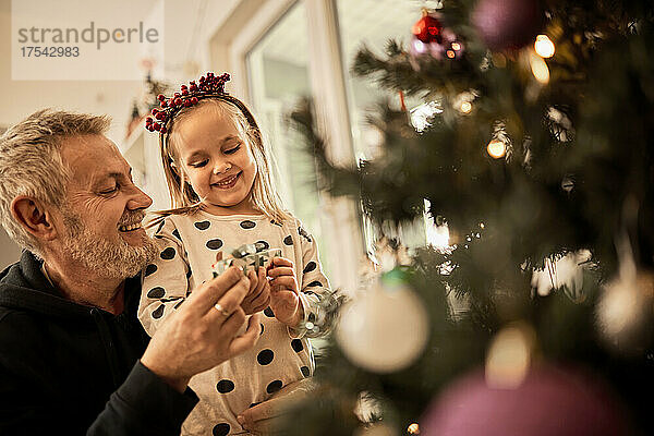 Grandfather and granddaughter decorating christmas tree at home