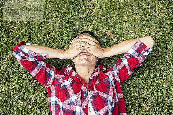 Woman covering eyes with hands lying on grass