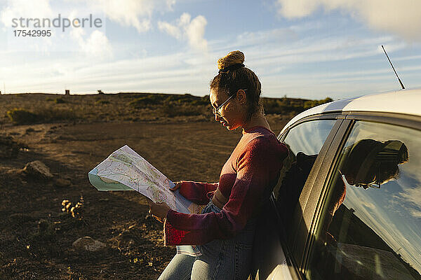 Frau mit Karte lehnt bei Sonnenuntergang an Auto