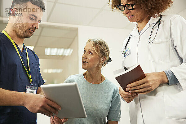 Patient diskutiert mit Krankenschwester  die einen Tablet-PC in der Hand hält  beim Arzt im Behandlungszimmer