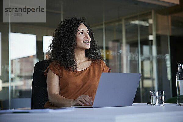 Glückliche Geschäftsfrau mit Laptop am Schreibtisch  die im Büro träumt