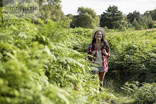 Smiling woman walking amidst green plants at Cannock Chase on sunny day