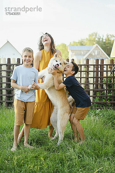Cheerful family with their Akita dog standing on grass in front of fence