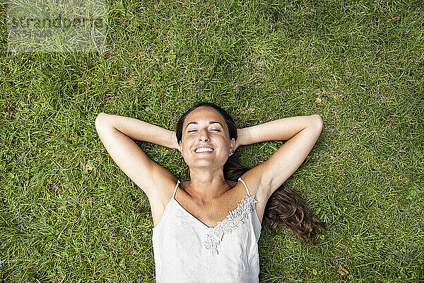 Lächelnde Frau mit den Händen hinter dem Kopf im Gras liegend
