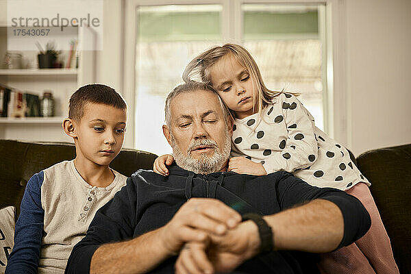 Großvater benutzt Smartwatch und sitzt mit Enkelkindern zu Hause